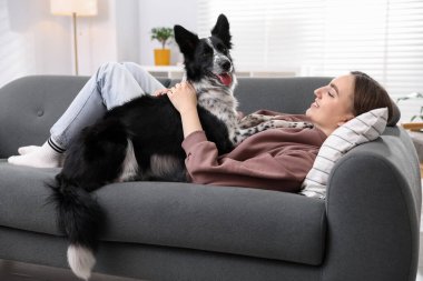 Evdeki kanepede sevimli köpeğiyle gülümseyen kadın.