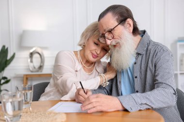 Ahşap masada son arzuları ve vasiyetnameleri imzalayan yaşlı çift.