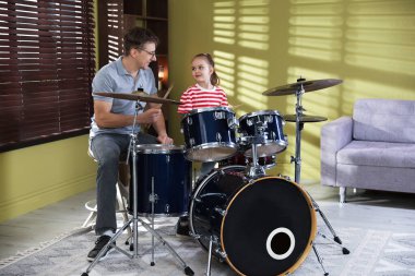 Küçük kız içeride müzik öğretmeniyle davul çalmayı öğreniyor.