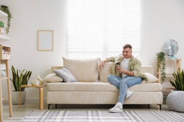 Akıllı telefonlu genç adam evdeki kanepede dinleniyor, mesaj atmak için yer var.