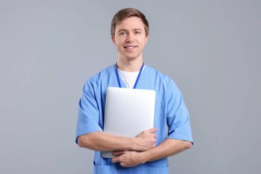 Gri arka planda dizüstü bilgisayarı olan bir tıp asistanı portresi