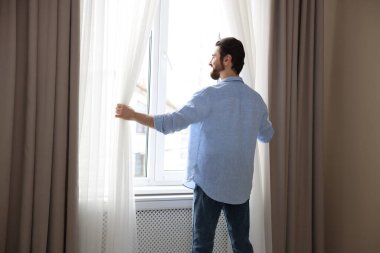 Evde şık pencere perdeleri açan adam