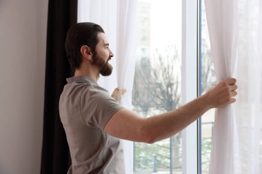 Evde şık pencere perdeleri açan adam