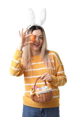 Paskalya kutlaması. Saç bandı takmış, tavşan kulaklı, hasırdan sepet dolusu beyaz arka planda boyalı yumurtaları olan gülümseyen bir kadın.