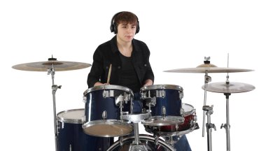 Kulaklıklı, bagetleriyle davul çalmayı öğrenen genç bir çocuk.