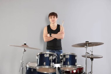 Gri arka planda bagetleri ve davul seti olan genç bir çocuk.