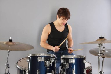 Gri arka planda davul çalmayı öğrenen güler yüzlü genç çocuk.