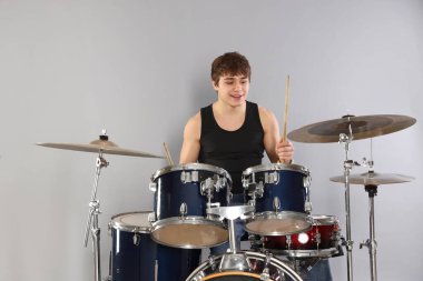 Gri arka planda davul çalmayı öğrenen güler yüzlü genç çocuk.