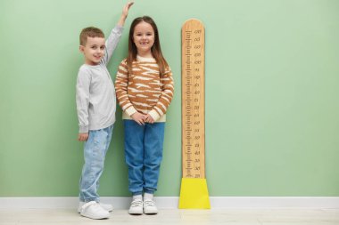 Küçük bir çocuk ve kız açık yeşil duvarın yanında boylarını grafikle ölçüyorlar.