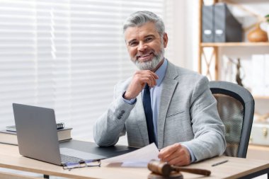 Takım elbiseli gülümseyen noterin portresi masadaki belge ve dizüstü bilgisayarla.