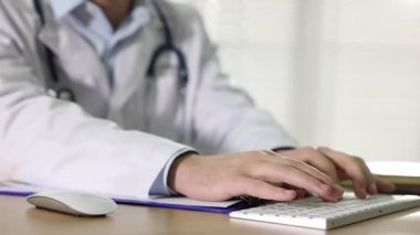 Tıp çalışanı bilgisayarını kullanıyor ve kapalı bir masadaki panoya yazı yazıyor.