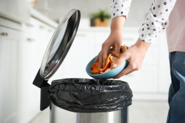 Mandalina kabuklarını mutfaktaki çöp kutusuna atan kadın, yakın plan.