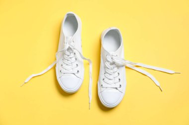 Sarı arka planda şık bir çift spor ayakkabı, üst manzara.