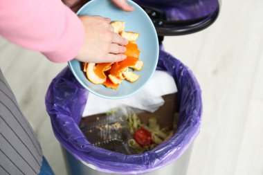 Kadın mutfaktaki çöp kutusuna elma kabuğu atıyor, yakın plan.