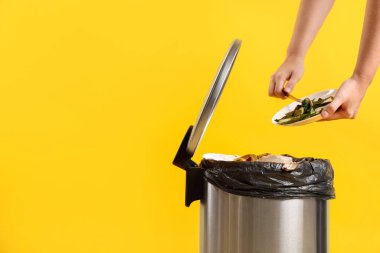 Sarı arka planda salatalık kabuklarını çöp kutusuna atan kadın, yakın plan. Metin için boşluk