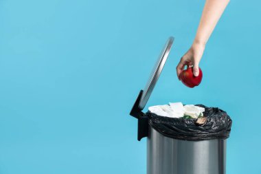 Açık mavi arka planda, çöp kutusuna elma atan kadın, yakın plan. Metin için boşluk