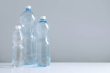 Beyaz masada gri arkaplan ile farklı boyutlarda su şişeleri, metin için boşluk