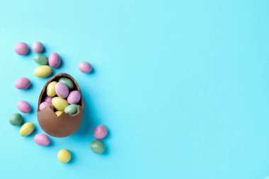 Paskalya kutlaması. Açık mavi arka planda şekerli kırık çikolata yumurtası, düz. Metin için boşluk