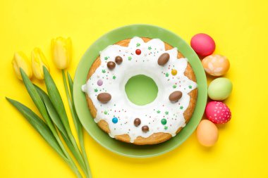 Lezzetli Paskalya pastası, boyanmış yumurtalar ve sarı arka planda güzel laleler, düz uzanma