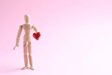 Pembe arka planda kırmızı kalpli ahşap manken, metin için yer