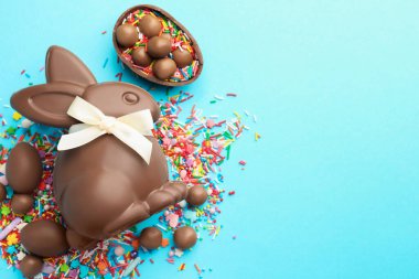 Çikolatalı Paskalya tavşanı, şekerli yumurta ve açık mavi arka planda serpiştirilmiş çikolata, düz yatak. Metin için boşluk