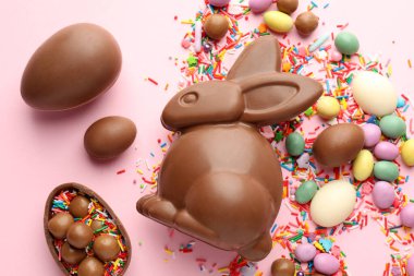 Çikolatalı Paskalya tavşanı, yumurtalar, şekerler ve pembe arka planda serpiştirilmiş şekerler.