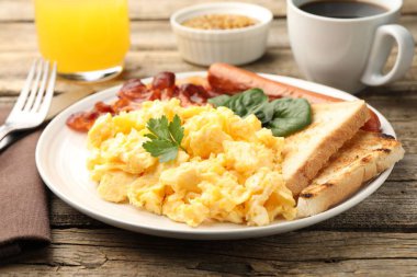 Lezzetli bir kahvaltı. Lezzetli çırpılmış yumurta, domuz pastırması ve sosis, ahşap masada servis edilir, yakın plan.