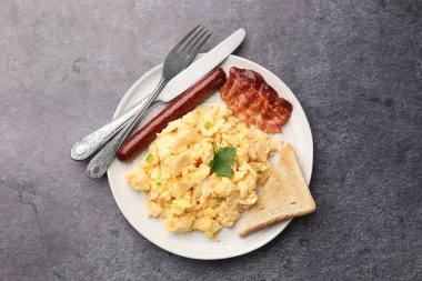 Lezzetli bir kahvaltı. Lezzetli çırpılmış yumurta, domuz pastırması, sosis ve ekmek gri desenli masada servis edilir.