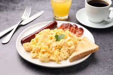 Lezzetli bir kahvaltı. Yağda yumurta, domuz pastırması, sosis ve ekmek. Gri desenli masada servis ediliyor. Yakın plan.