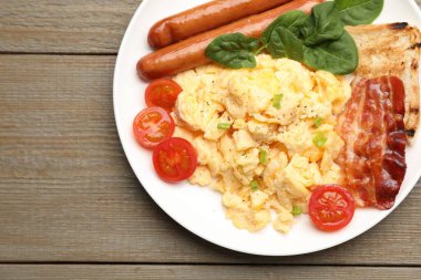 Lezzetli bir kahvaltı. Lezzetli çırpılmış yumurta, domuz pastırması, sosis ve domatesler ahşap masada servis edilir, üst manzara. Metin için boşluk