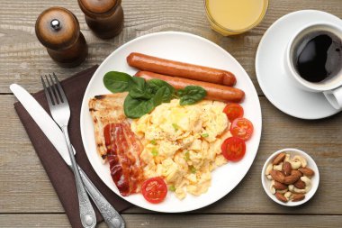 Lezzetli bir kahvaltı. Lezzetli çırpılmış yumurta, domuz pastırması, sosis ve domatesler ahşap masada servis ediliyor.