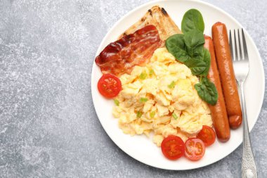 Lezzetli bir kahvaltı. Lezzetli çırpılmış yumurta, domuz pastırması, sosis ve domates. Gri desenli masa, üst manzara. Metin için boşluk