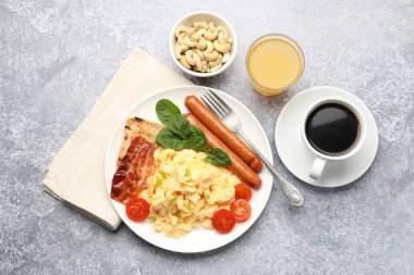 Lezzetli bir kahvaltı. Lezzetli çırpılmış yumurta, domuz pastırması, sosis ve domatesler gri dokuma masasında servis ediliyor.