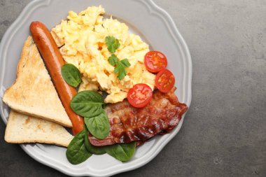Lezzetli bir kahvaltı. Lezzetli omlet, domuz pastırması, sosis ve domatesler gri dokuma masasında servis edilir. Metin için boşluk