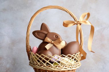 Çikolatalı Paskalya tavşanı ve hasır sepette yumurtalar açık gri arka planda, yakın plan.