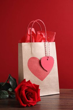 Kağıt torba ve gül ahşap masada kırmızı arka planda.