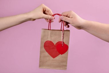 Sevgililer Günü hediyesi pembe arka planda olan kadın kesekağıdı veren adam, yakın plan.