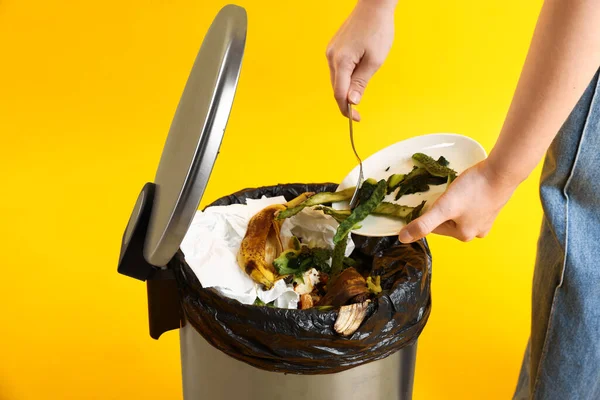 Sarı arka planda salatalık kabuklarını çöp kutusuna atan kadın, yakın plan.