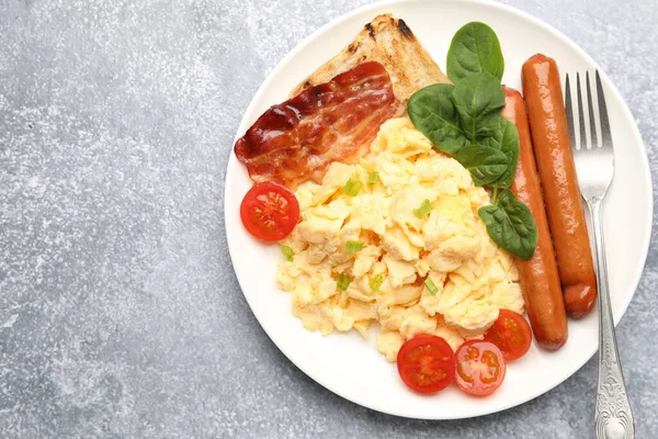 Lezzetli bir kahvaltı. Lezzetli çırpılmış yumurta, domuz pastırması, sosis ve domates. Gri desenli masa, üst manzara. Metin için boşluk
