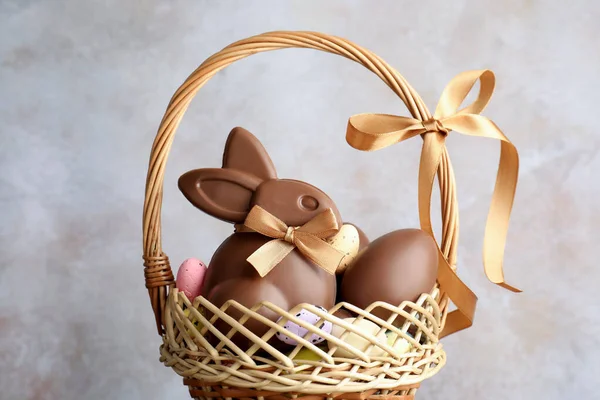 Çikolatalı Paskalya tavşanı ve hasır sepette yumurtalar açık gri arka planda, yakın plan.