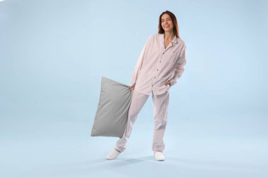 Açık mavi arka planda yastıklı şık pijamalı güzel bir kadın.