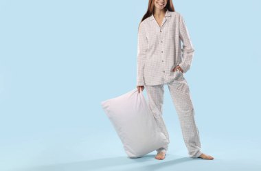 Açık mavi arka planda yastıklı şık pijamalı güzel kadın, yakın plan.