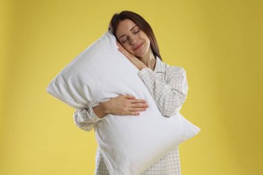 Sarı arka planda yastıklı şık pijamalı güzel bir kadın.