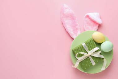 Boyalı Paskalya yumurtaları, tavşan kulaklığı ve pembe arka planda hediye, üst manzara. Metin için boşluk
