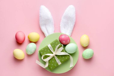 Boyalı Paskalya yumurtaları, tavşan kulaklığı ve pembe arka planda hediye, düz uzanma.