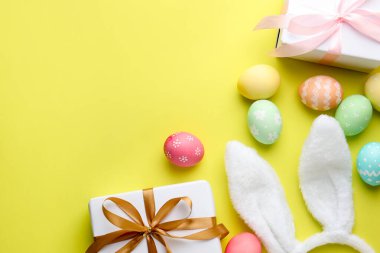 Boyalı Paskalya yumurtaları, tavşan kulaklıkları açık yeşil arka planda hediyeler, düz yatak. Metin için boşluk