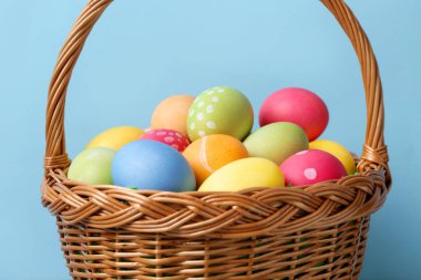 Hasır sepette boyalı Paskalya yumurtaları açık mavi arkaplan, yakın plan.