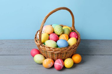 Hasır sepetin içine boyanmış Paskalya yumurtaları açık mavi arka plana karşı gri ahşap masa üzerinde