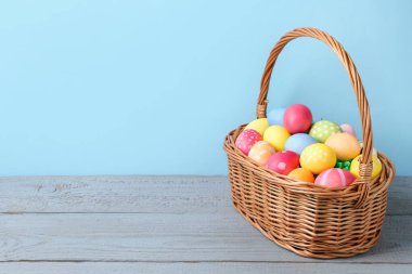 Hasır sepetin içine boyanmış Paskalya yumurtaları açık mavi arka planda gri ahşap masa üzerinde. Metin için boşluk