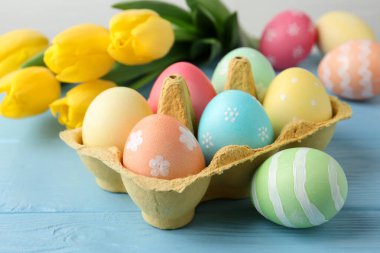 Kutuda boyanmış Paskalya yumurtaları ve açık mavi ahşap masa üzerinde güzel laleler. Yakın plan.